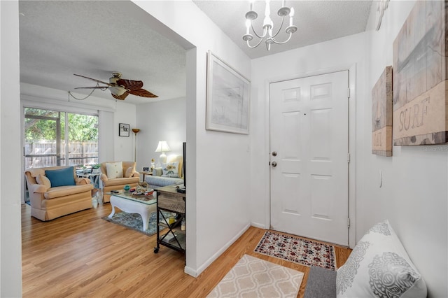 foyer entrance with light wood-type flooring, a textured ceiling, a chandelier, a ceiling fan, and baseboards