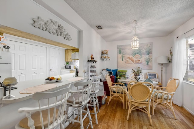 dining space with a textured ceiling, light wood-type flooring, and a chandelier