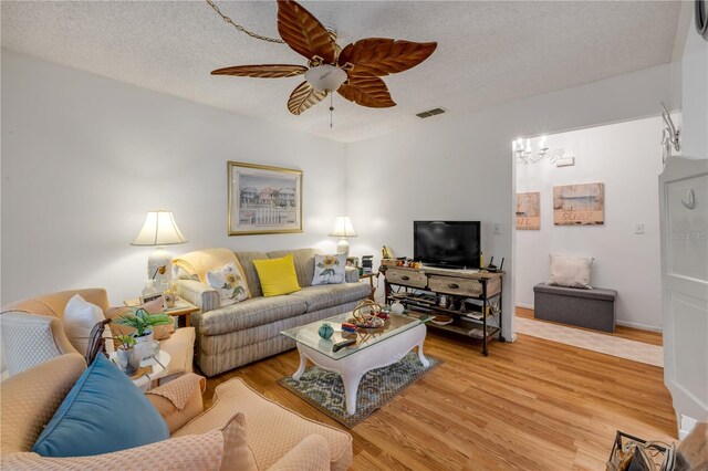 living room featuring light wood finished floors, ceiling fan, and a textured ceiling