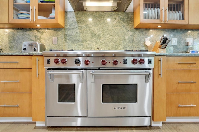 kitchen featuring range with two ovens, range hood, light stone counters, and decorative backsplash