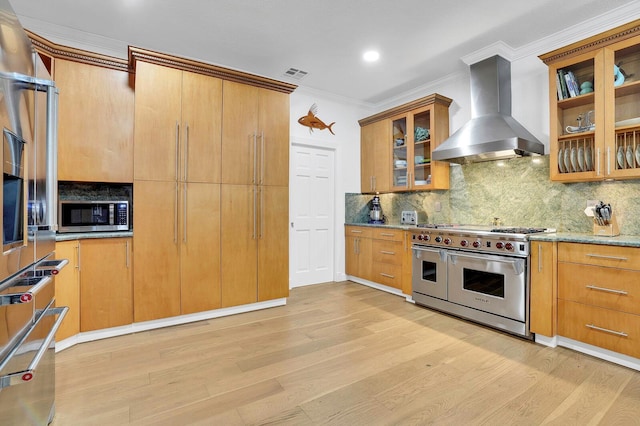 kitchen with appliances with stainless steel finishes, wall chimney exhaust hood, light wood-type flooring, ornamental molding, and decorative backsplash