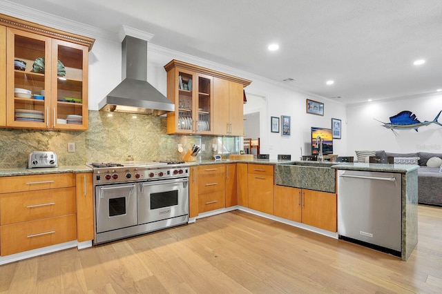 kitchen featuring appliances with stainless steel finishes, wall chimney range hood, open floor plan, ornamental molding, and a peninsula