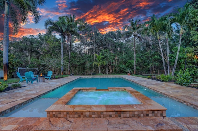 pool at dusk featuring a patio area, a pool with connected hot tub, and fence