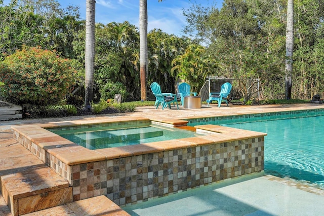 view of swimming pool with a pool with connected hot tub, view of wooded area, and a patio