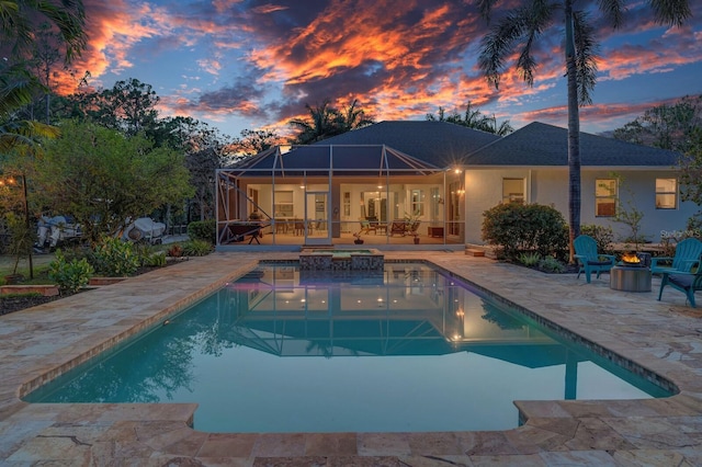 back of property at dusk featuring a patio, an outdoor fire pit, glass enclosure, an outdoor pool, and stucco siding