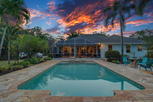 back of property at dusk with a patio, an outdoor fire pit, a lanai, an outdoor pool, and stucco siding