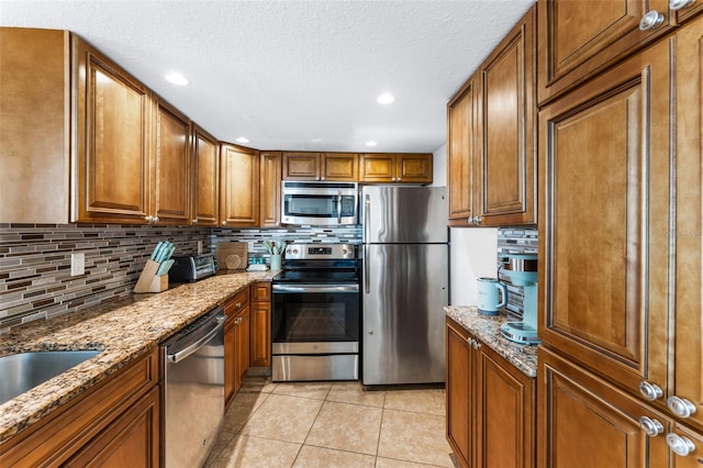 2625 S Atlantic Ave Unit 18Nw, Daytona Beach, FL 32118 - kitchen featuring stainless steel appliances, light tile patterned floors, decorative backsplash, brown cabinets, and stone counters