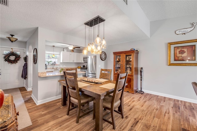 1205 Bond St, Edgewater, FL 32132 - dining area featuring a textured ceiling, light wood-style floors, a chandelier, baseboards, and a ceiling fan