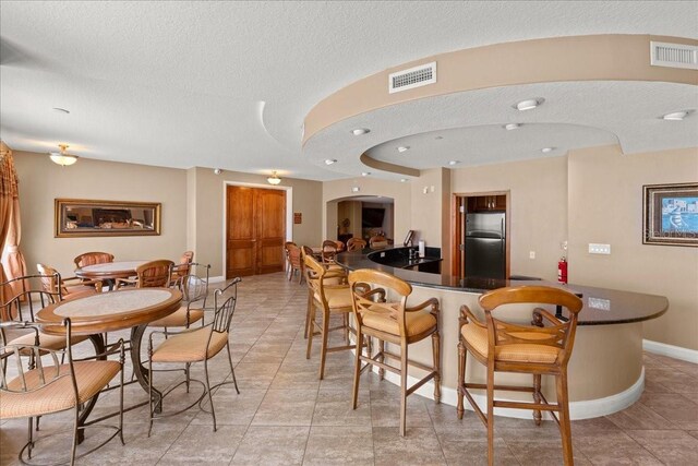 3245 S Atlantic Ave Unit 208, Daytona Beach, FL 32118 - kitchen featuring freestanding refrigerator, dark countertops, a kitchen bar, arched walkways, and light tile patterned flooring