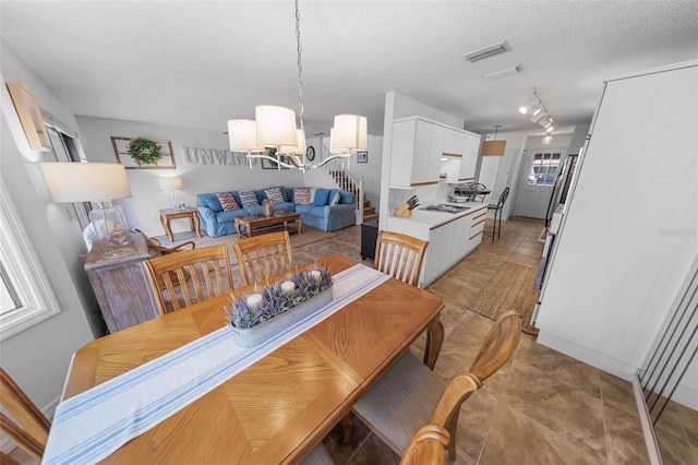 2961 Oceans Trce, Daytona Beach Shores, FL 32118 - dining room with a chandelier, stairway, rail lighting, a textured ceiling, and light tile patterned floors