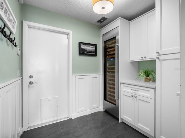 1215 Commodore Dr, New Smyrna Beach, FL 32168 - kitchen featuring beverage cooler, light countertops, white cabinets, wainscoting, and a textured ceiling