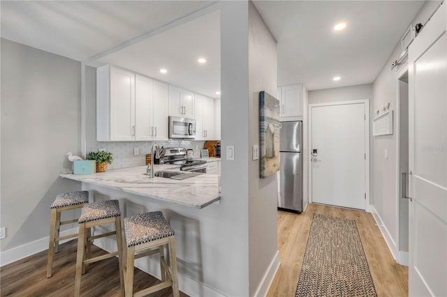 4151 S Atlantic Ave Unit 3090, New Smyrna Beach, FL 32169 - kitchen with appliances with stainless steel finishes, light wood-style floors, white cabinetry, a kitchen bar, and light stone countertops