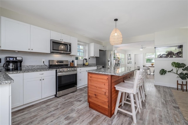 653 Goodwin Ave, New Smyrna Beach, FL 32169 - kitchen featuring appliances with stainless steel finishes, light wood finished floors, white cabinetry, and a kitchen bar