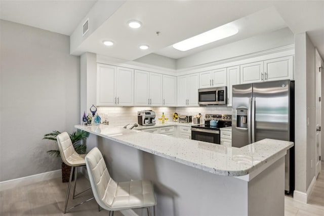 7 Riverwalk Dr Unit 305, New Smyrna Beach, FL 32169 - kitchen featuring appliances with stainless steel finishes, a peninsula, baseboards, backsplash, and white cabinetry