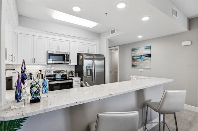 7 Riverwalk Dr Unit 305, New Smyrna Beach, FL 32169 - kitchen featuring appliances with stainless steel finishes, a peninsula, light stone counters, a breakfast bar area, and white cabinets