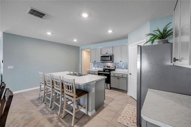 2731 Neverland Dr, New Smyrna Beach, FL 32168 - kitchen featuring appliances with stainless steel finishes, gray cabinets, an island with sink, light tile patterned floors, and a kitchen bar