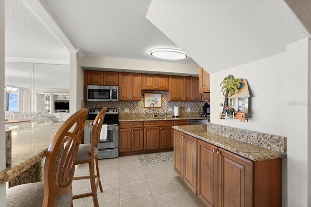 901 S Atlantic Ave Unit 202, Ormond Beach, FL 32176 - kitchen with stainless steel appliances, brown cabinets, backsplash, light stone counters, and light tile patterned floors
