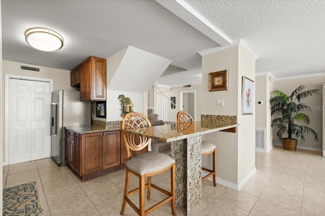 901 S Atlantic Ave Unit 202, Ormond Beach, FL 32176 - kitchen with brown cabinetry, a breakfast bar, light tile patterned flooring, stainless steel fridge with ice dispenser, and a textured ceiling