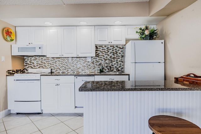 3700 S Atlantic Ave Unit 108, New Smyrna Beach, FL 32169 - kitchen with white appliances, light tile patterned floors, white cabinetry, tasteful backsplash, and dark stone counters