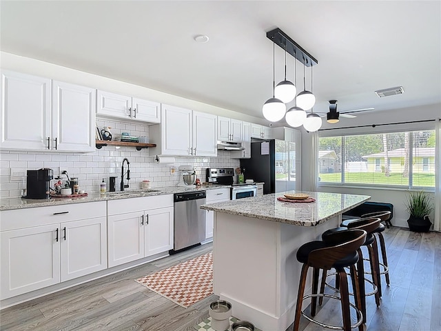 1421 Pine Tree Dr, Edgewater, FL 32132 - kitchen with appliances with stainless steel finishes, under cabinet range hood, ceiling fan, a center island, and light wood-type flooring
