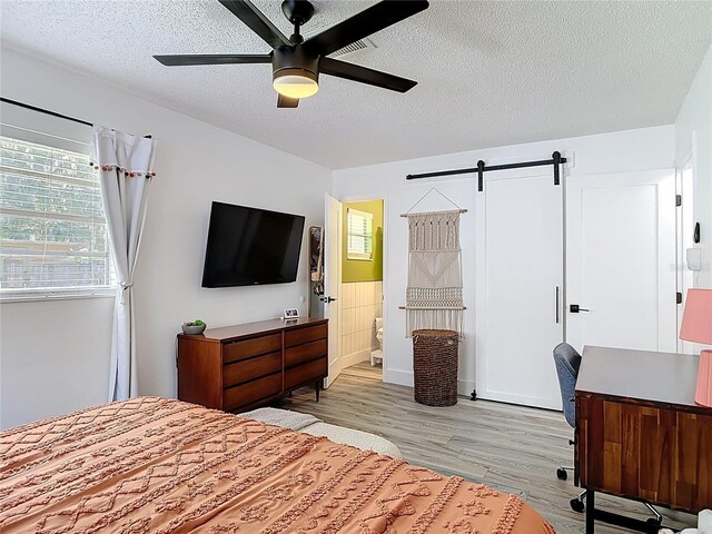 1421 Pine Tree Dr, Edgewater, FL 32132 - bedroom with a textured ceiling, light wood-style floors, a barn door, and a ceiling fan