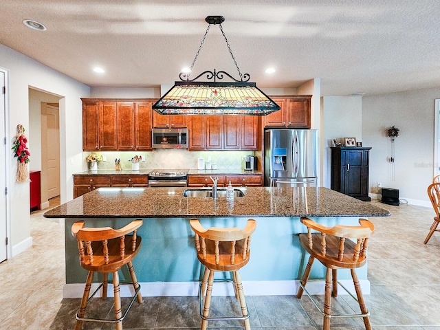 6804 Forkmead Ln, Port Orange, FL 32128 - kitchen featuring appliances with stainless steel finishes, a breakfast bar, a kitchen island with sink, brown cabinetry, and a textured ceiling