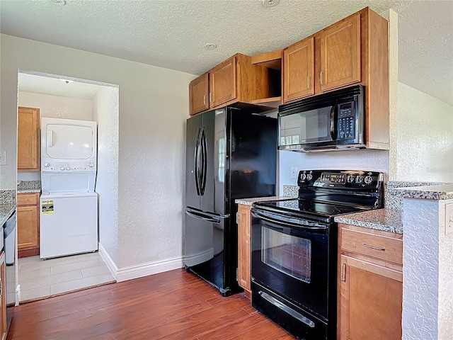 3045 Pine Tree Dr, Edgewater, FL 32141 - kitchen with black appliances, estacked washer and dryer, light wood-style floors, brown cabinetry, and a textured ceiling