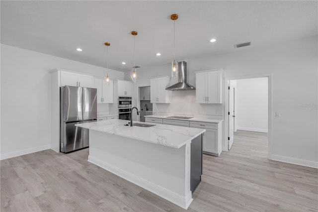 2324 Orange Tree Dr, Edgewater, FL 32141 - kitchen featuring appliances with stainless steel finishes, wall chimney range hood, an island with sink, white cabinets, and light wood-type flooring