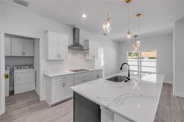 2324 Orange Tree Dr, Edgewater, FL 32141 - kitchen with wall chimney exhaust hood, black electric stovetop, independent washer and dryer, an island with sink, and light wood-type flooring