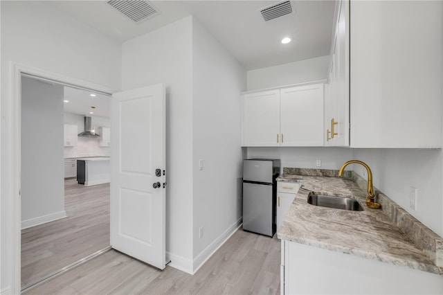 2324 Orange Tree Dr, Edgewater, FL 32141 - kitchen with freestanding refrigerator, wall chimney exhaust hood, white cabinets, light wood-type flooring, and light stone countertops