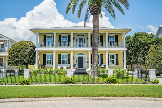 1212 S Riverside Dr, New Smyrna Beach, FL 32168 - neoclassical / greek revival house with a balcony, covered porch, stucco siding, a standing seam roof, and a fenced front yard