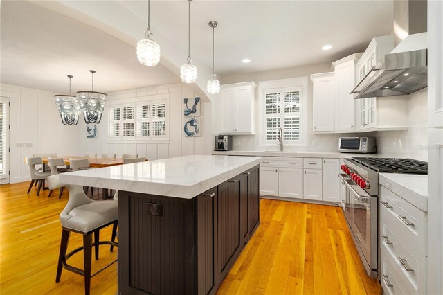 1212 S Riverside Dr, New Smyrna Beach, FL 32168 - kitchen with wall chimney range hood, appliances with stainless steel finishes, white cabinetry, light wood-style flooring, and recessed lighting