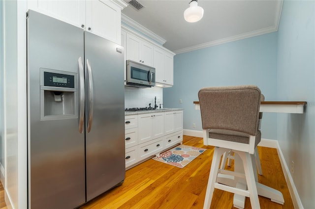 1212 S Riverside Dr, New Smyrna Beach, FL 32168 - kitchen featuring stainless steel appliances, crown molding, backsplash, white cabinetry, and light wood-style floors