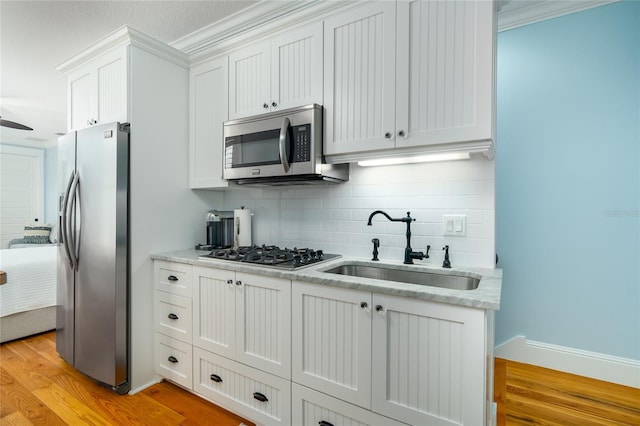 1212 S Riverside Dr, New Smyrna Beach, FL 32168 - kitchen with appliances with stainless steel finishes, backsplash, light wood-style flooring, white cabinetry, and ornamental molding