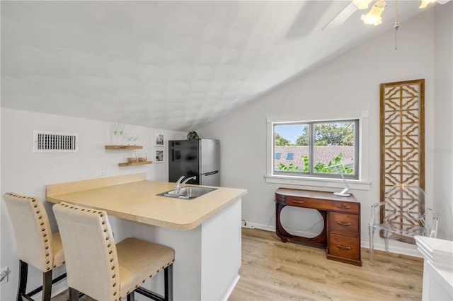 1219 Commodore Dr, New Smyrna Beach, FL 32168 - kitchen with freestanding refrigerator, vaulted ceiling, light wood finished floors, a peninsula, and light countertops