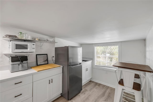 402 N Orange St, New Smyrna Beach, FL 32168 - kitchen featuring white microwave, freestanding refrigerator, light wood-type flooring, light countertops, and white cabinets