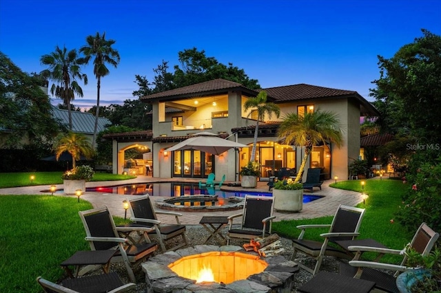 206 Canova Dr, New Smyrna Beach, FL 32169 - back of property at dusk featuring a fire pit, stucco siding, a balcony, an outdoor pool, and a patio