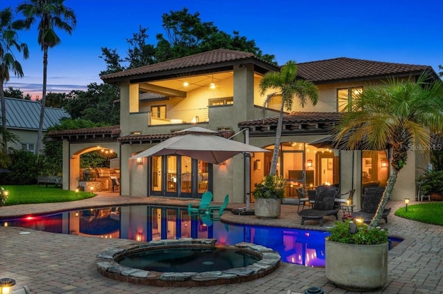 206 Canova Dr, New Smyrna Beach, FL 32169 - back of property at dusk featuring a patio, a pool with connected hot tub, stucco siding, and a tile roof