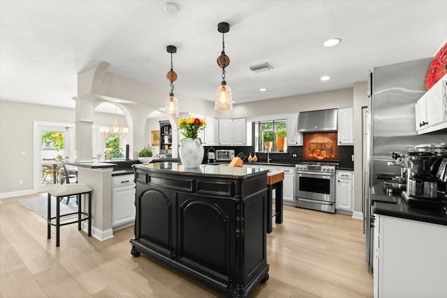 206 Canova Dr, New Smyrna Beach, FL 32169 - kitchen with appliances with stainless steel finishes, a kitchen island, dark countertops, white cabinetry, and wall chimney range hood
