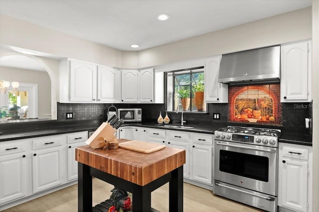 206 Canova Dr, New Smyrna Beach, FL 32169 - kitchen with stainless steel appliances, wall chimney range hood, dark countertops, white cabinets, and tasteful backsplash