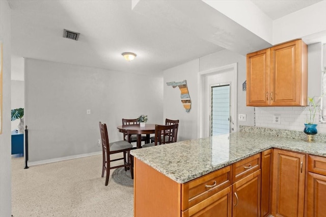 211 Fox Pl, Port Orange, FL 32127 - kitchen featuring backsplash, light stone countertops, a peninsula, and brown cabinets