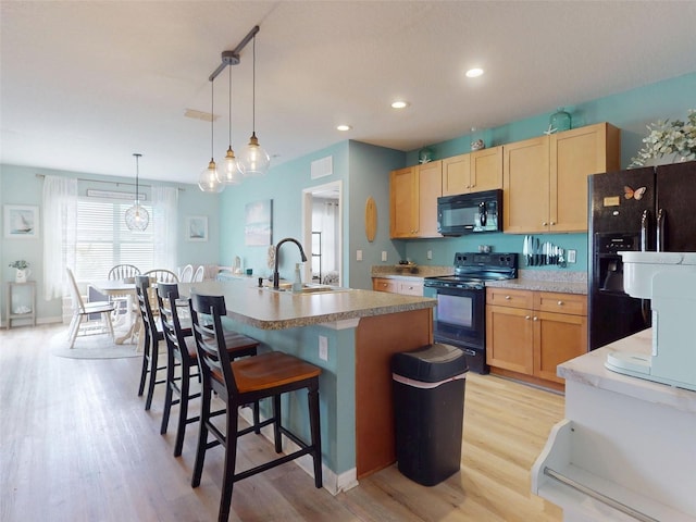2731 Star Coral Ln, New Smyrna Beach, FL 32168 - kitchen with black appliances, light wood-style flooring, light brown cabinetry, a center island with sink, and a breakfast bar