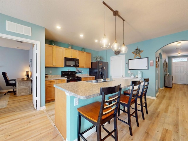 2731 Star Coral Ln, New Smyrna Beach, FL 32168 - kitchen featuring black appliances, light wood finished floors, light countertops, arched walkways, and an island with sink