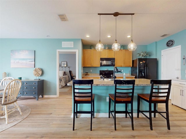 2731 Star Coral Ln, New Smyrna Beach, FL 32168 - kitchen with black appliances, light wood-type flooring, recessed lighting, a center island with sink, and a kitchen bar