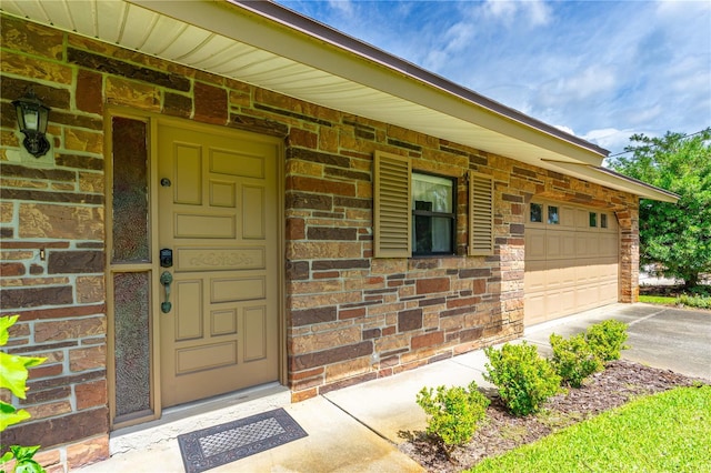 view of exterior entry with driveway, brick siding, and an attached garage