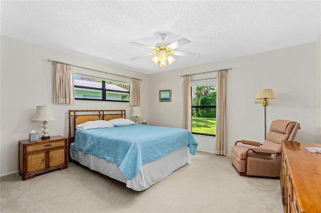 bedroom with light carpet, multiple windows, a ceiling fan, and a textured ceiling