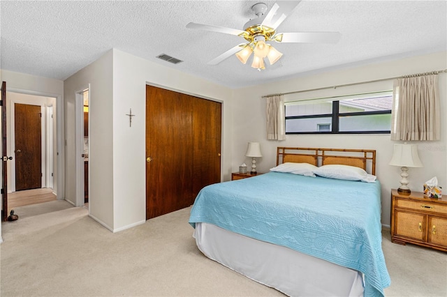 bedroom with light colored carpet, a closet, a textured ceiling, and a ceiling fan