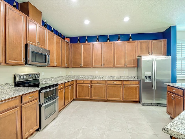 3361 Pegaso Ave, New Smyrna Beach, FL 32168 - kitchen featuring appliances with stainless steel finishes, brown cabinetry, a textured ceiling, light stone countertops, and recessed lighting