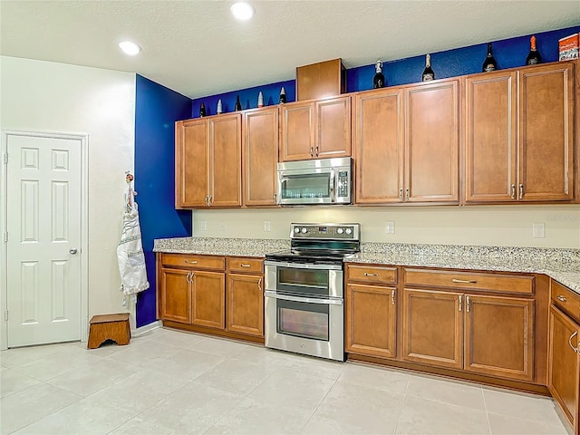 3361 Pegaso Ave, New Smyrna Beach, FL 32168 - kitchen with appliances with stainless steel finishes, brown cabinets, light stone countertops, light tile patterned floors, and recessed lighting