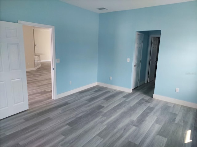 empty room with wood finished floors, visible vents, and baseboards